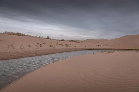 Dramatic sky over the never-ending sand dunes and river of the Gobi desert .. Stock Photos