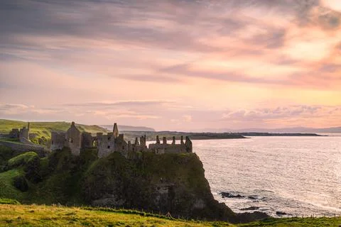 Dramatic sky over ruins of Dunluce Castle perched on the edge of cliff, North Stock Photos