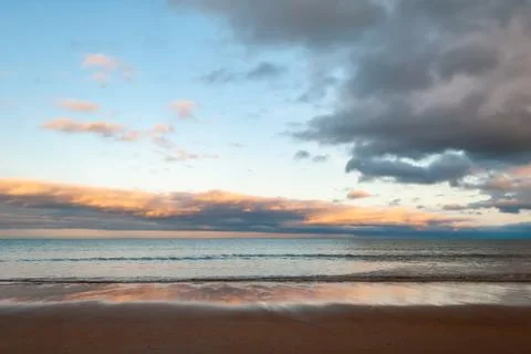 Dramatic sky over the sea as waves gently lap onto the beach in the golden li Stock Photos
