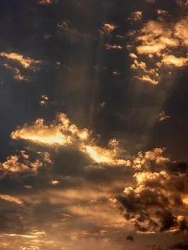 Dramatic sky scene with sun rays piercing through golden clouds at dusk Stock Photos