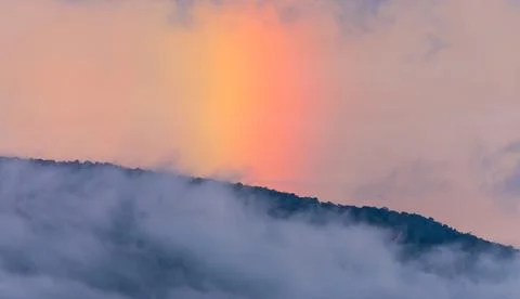 Dramatic sky shining rainbow behind the foggy mountain at twilight. Foto stock
