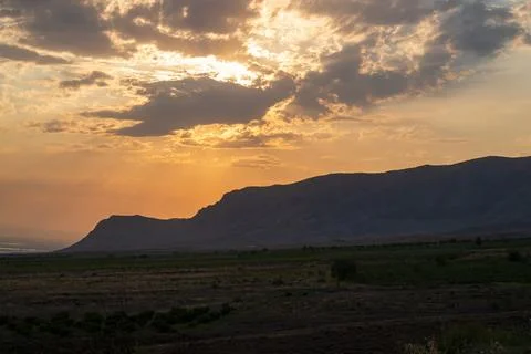 Dramatic sky with sun peeking through clouds above barren hills 库存照片