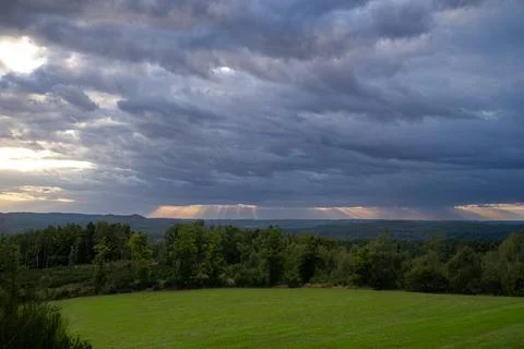 Dramatic sky with sun rays over green landscape. Stock Photos