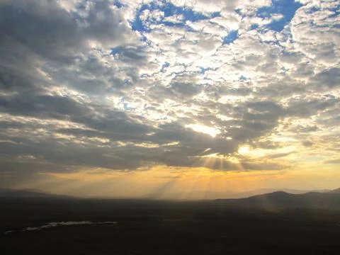 Dramatic sky with sunbeams breaking through clouds over a serene landscape. Stock Photos