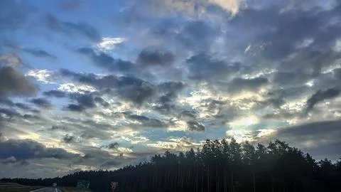 Dramatic sky with sunbeams breaking through dark clouds over a forest Stock Photos
