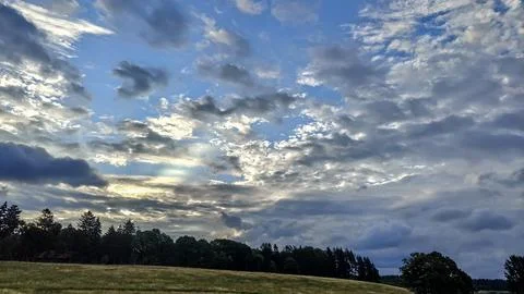 Dramatic sky with sunbeams breaking through clouds over a grassy field Stock Photos