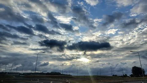 Dramatic sky with sunbeams breaking through dark clouds over a highway Stock Photos