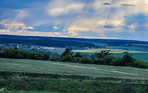 Dramatic sky with sunbeams over rolling green hills and a distant village Fotos Stock