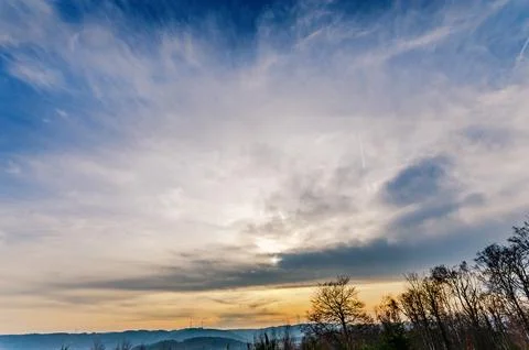 Dramatic sky with wispy clouds and distant hills at sunset Stock Photos