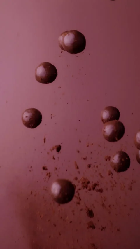 A dramatic slow-motion shot of chocolate balls exploding and scattering, with Stock Footage 295334197