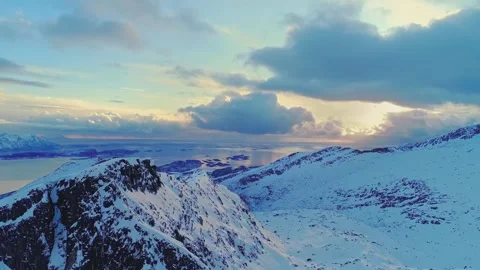 Dramatic snow peaked mountains overlooking arctic ocean fjords during golden Stock Footage 345484154
