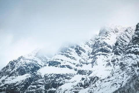 Dramatic snowy mountain peaks partially covered in fog create a raw winter .. Fotos Stock