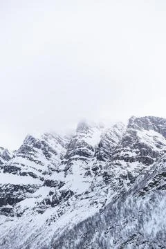 Dramatic snowy mountain peaks partially covered in fog create a raw winter .. Foto stock