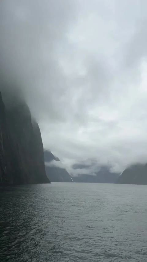 Dramatic steep cliffs rising from the dark waters of milford sound in new Vídeos de archivo 334163513