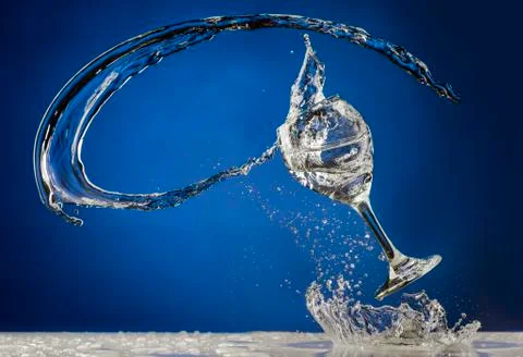 Dramatic stop motion liquid spilling from wine glass on blue background Stock Photos