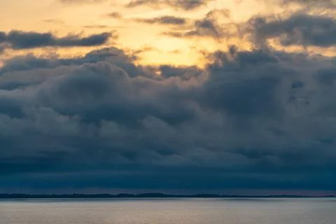 Dramatic storm clouds above sea water surface with golden sunrise behind the Stock Photos