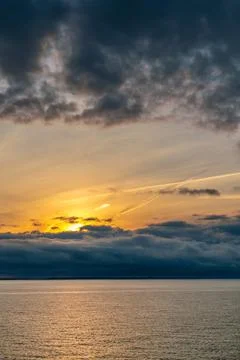 Dramatic storm clouds above sea water surface with golden sunrise behind the Stock Photos