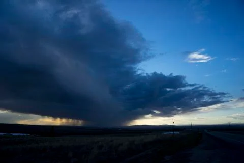 Dramatic storm clouds and falling rain on the horizon glowing with sunlight at s Stock Photos