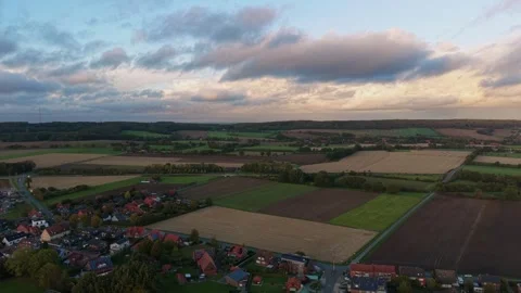 Dramatic storm clouds drift above patchwork farm fields bordering small Stock Footage 348083190