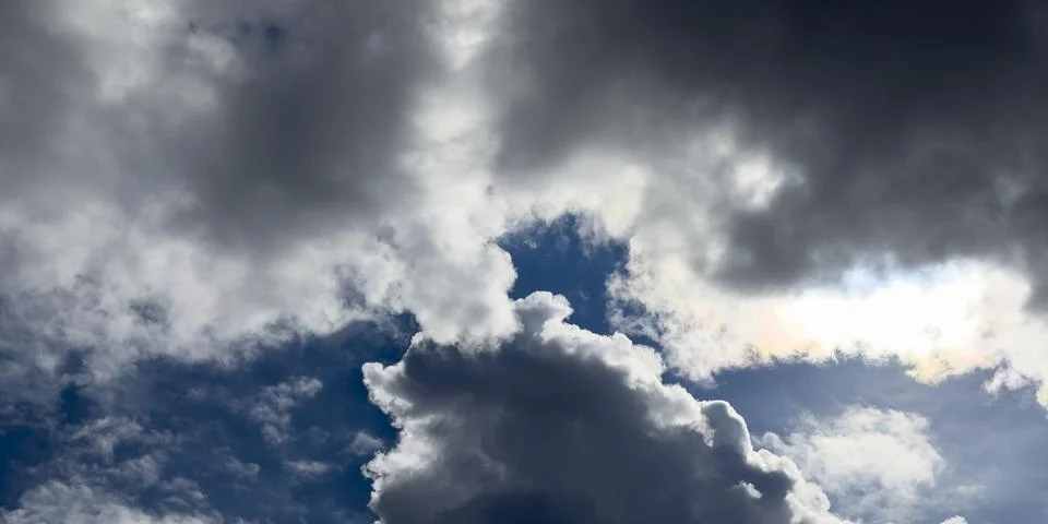 Dramatic storm clouds fill a dark blue sky. Sunlight breaks through the cloud Stock Photos