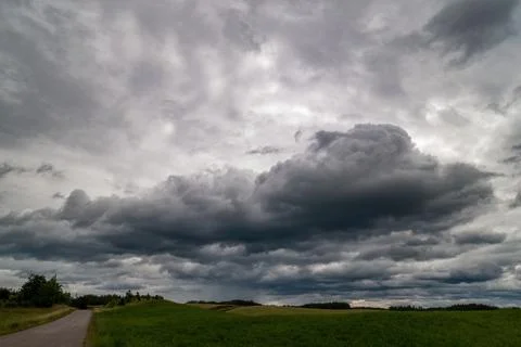 Dramatic storm clouds gather over a rural landscape with a narrow road Stock Photos