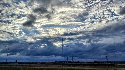 Dramatic storm clouds gather over a highway with streetlights at dusk Foto stock