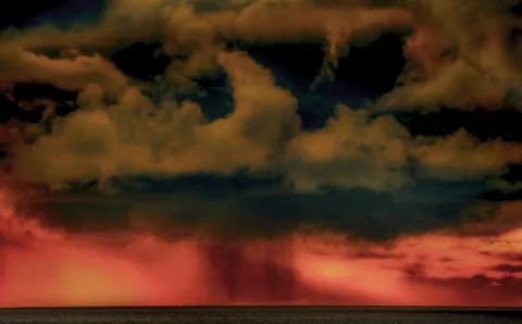 Dramatic storm clouds gather over a fiery red sunset horizon 스톡 사진