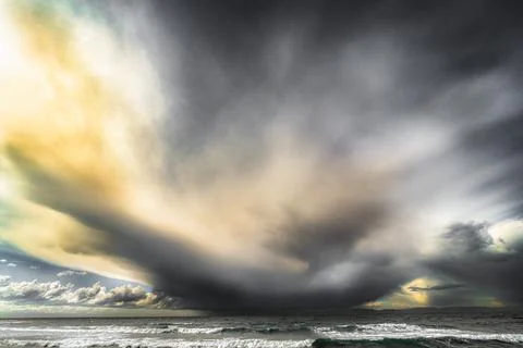 Dramatic storm clouds gather over the ocean with waves crashing on the shore 스톡 사진