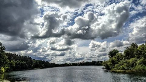 Dramatic storm clouds gather over a serene lake and lush green forest landsca 写真素材