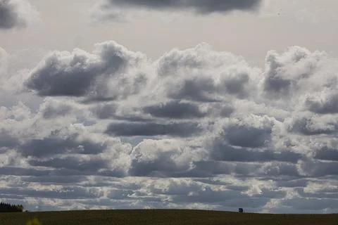 Dramatic storm clouds gather over a vast green field with a distant structure Stock Photos