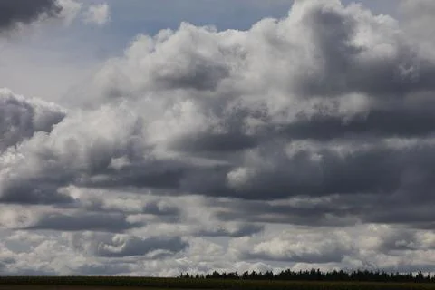 Dramatic storm clouds gather over a distant tree line and field Stock Photos