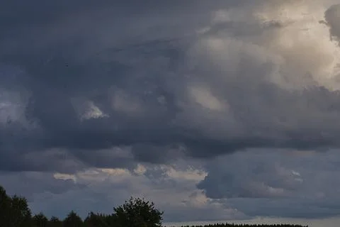 Dramatic storm clouds gather over a dark forest landscape Stock Photos