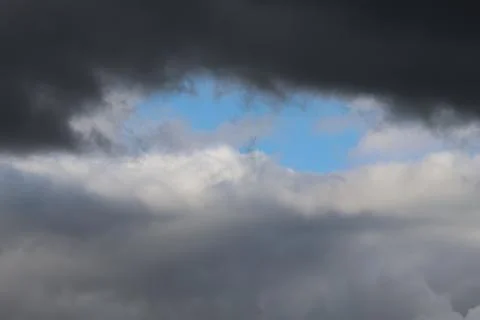 Dramatic storm clouds open to reveal a bright blue patch of sky above layer.. Stock Photos