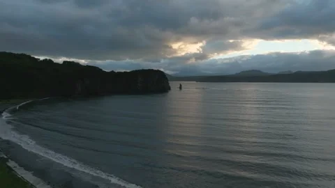 Dramatic storm clouds over calm bay and rocky coastline at dusk aerial view Stock Footage 336295387