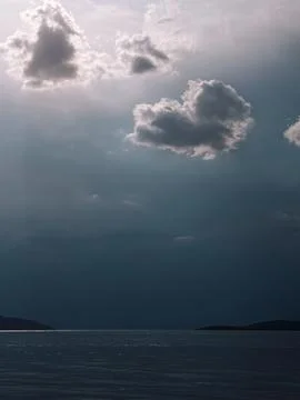 Dramatic storm clouds over calm sea with sun rays, moody coastal landscape Stock Photos