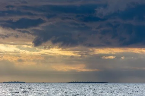 Dramatic storm clouds over the dark sea during sunset. Beautiful golden light 写真素材