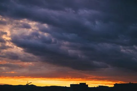 Dramatic storm clouds over fiery orange sunset city skyline silhouette Stock Photos