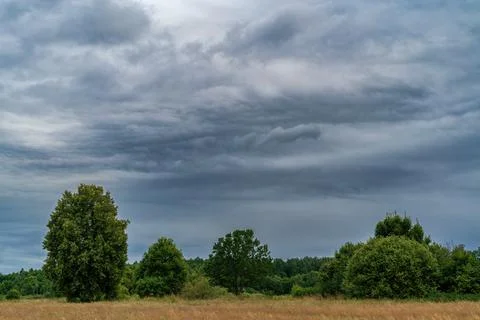 Dramatic storm clouds over a green countryside meadow and trees Stock Photos