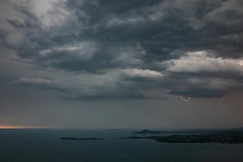 Dramatic storm clouds over a lake with low islands and dim glow along horizon Stockfoto's