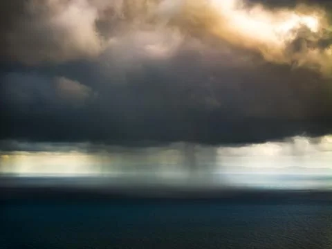 Dramatic storm clouds over the ocean with rain shafts and distant landmass Fotos de archivo
