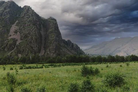Dramatic storm clouds over rocky mountain ridge and green valley in Altai 스톡 사진