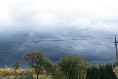 Dramatic Storm Clouds Over Trees and Power Lines Dark Blue Sky, Autumn Foliage 스톡 사진