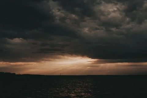 Dramatic storm clouds part above a dark horizon as warm sunlight Stock Photos