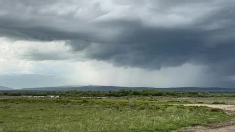 Dramatic Storm Clouds Releasing Rain Over Green Landscape and Mountains Stock Footage 339171497