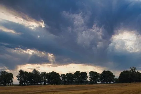 Dramatic storm clouds with sunbeams breaking through over a harvested field Fotos Stock