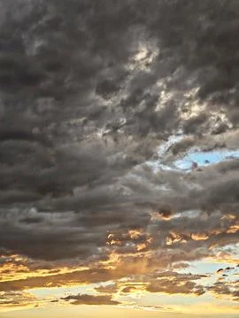 ​Dramatic storm clouds at sunset with a magical glow of blue and golden light. Stock Photos