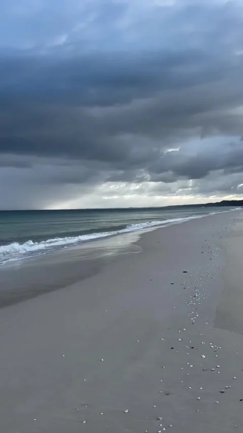 Dramatic stormy clouds over a peaceful sandy beach shoreline Vídeos de archivo 334084364