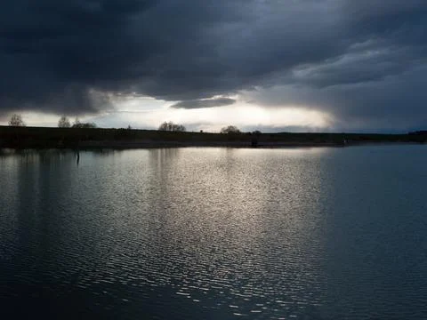 Dramatic stormy dark sky over the pond at spring, almost monochrome,siluette 스톡 사진