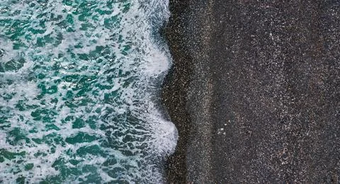 Dramatic stormy waves with white sea foam over black sand beach, aerial textu Stock Photos