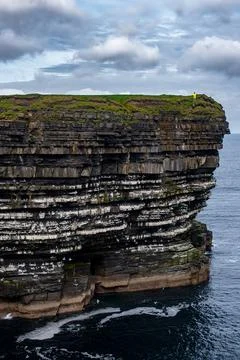 Dramatic stratified rock formations on the coast, green clifftop over the deep b Fotos Stock